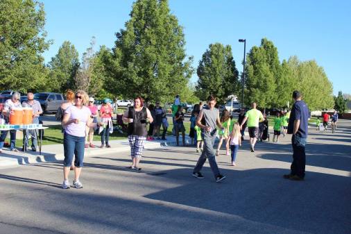 Families and runners mingle in a parking lot after the SoleKIDs race, under a row of trees at sunset